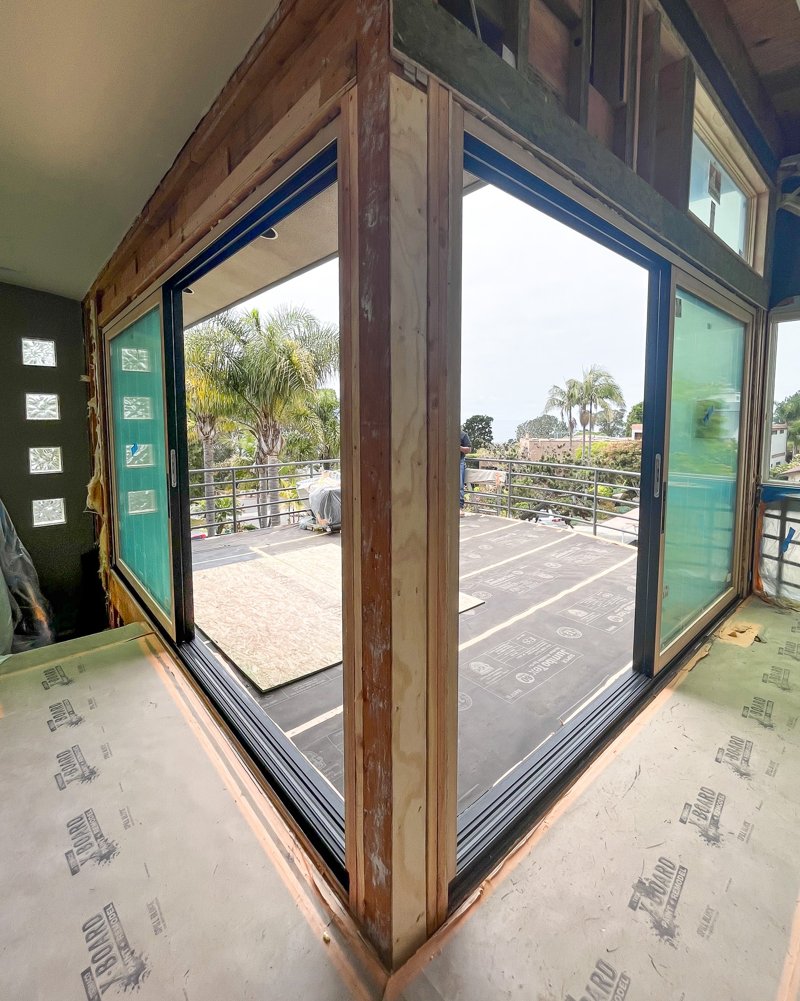 Untitled-324 View from inside a room under construction with open glass folding doors leading to a balcony overlooking a garden.